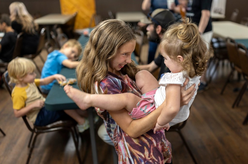 A young girl smiles at a toddler she's holding in her arms.