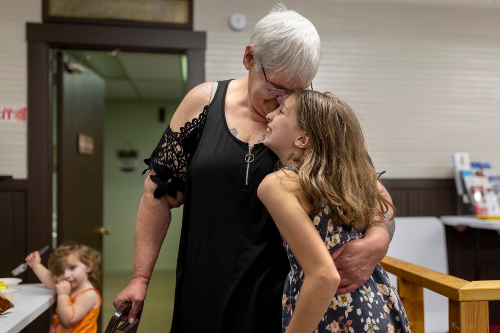 A woman hugs a grinnning young girl and presses her nose up against the girl's forehead.